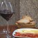 A wine glass set next to a bread basket and a plate of ham and cheese